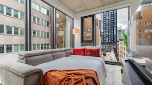 Un dormitori modern amb un llit gran, un sofà i vista a edificis alts.