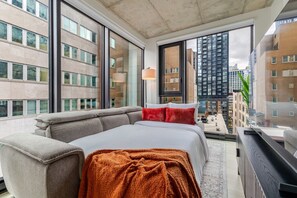 A modern bedroom with a large bed, a sofa, and a view of tall buildings. - Downtown Poolside Retreat | Free Parking & Pool (Montréal)