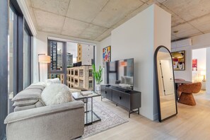 A modern living room with a sofa, TV, and a mirror. - Downtown Poolside Retreat | Free Parking & Pool (Montréal)