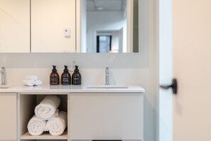A bathroom with a white vanity, a mirror, and three bottles of toiletries. - Downtown Poolside Retreat | Free Parking & Pool (Montréal)