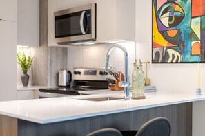 Eine moderne Küche mit Mikrowelle aus Edelstahl, einem Backofen, einer Spüle mit modernem Wasserhahn und einem farbenfrohen, abstrakten Gemälde an der Wand.