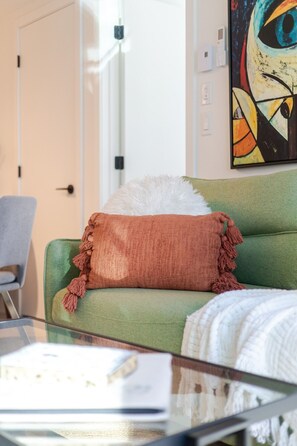 A green sofa with a brown cushion and tassels, a white fluffy pillow, and a glass coffee table with a magazine. - Modern Montreal Escape | Pools Gym Cinema Balcony (Montreal)