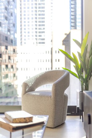 A modern room with a textured armchair, a potted plant, and a view of city buildings. - Modern Montreal Escape | Pools Gym Cinema Balcony (Montreal)