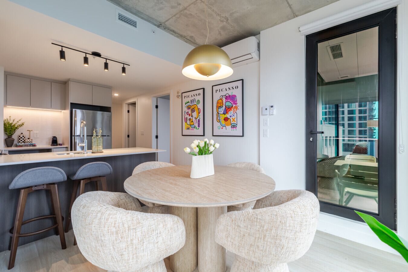 A modern kitchen with a central island, bar stools, and a dining table with a vase of flowers.