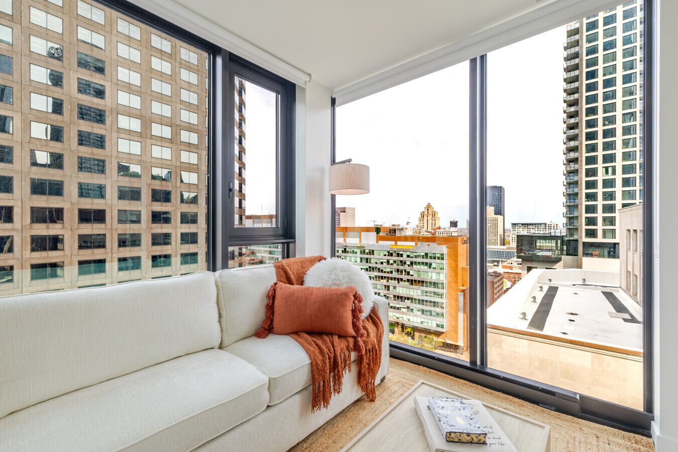 Een moderne woonkamer met een groot raam, een witte bank en uitzicht op stadsgebouwen.