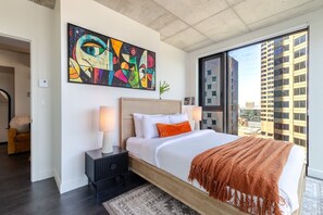 A modern hotel room with a large bed, two bedside lamps, a colorful abstract painting, and a city view. - Modern Escape | Free Parking & Rooftop Pool (Montréal)