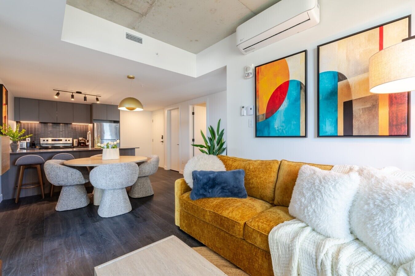 A modern living room with a sofa, a dining table with chairs, and a kitchen in the background.