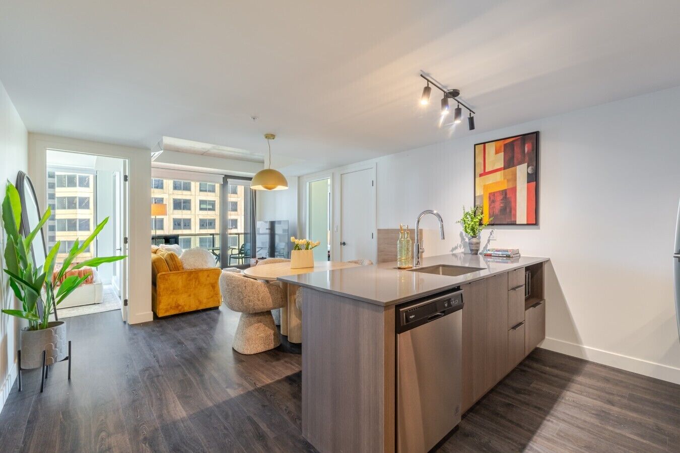 A modern kitchen with a central island, a dining area with a yellow sofa, and a large window offering a city view.