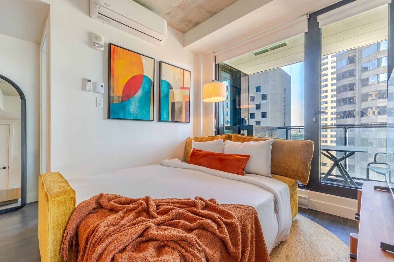 Een moderne hotelkamer met een groot bed, een balkon met uitzicht op de stad en abstracte kunst aan de muur.