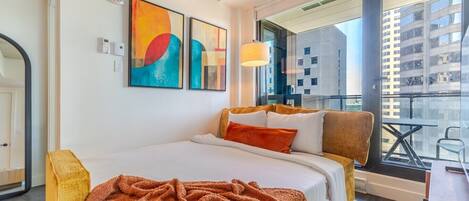 Habitación de hotel moderna con una cama grande, un balcón con vistas a la ciudad y arte abstracto en la pared.