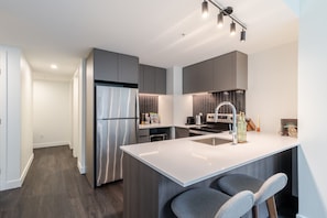 A modern kitchen with a stainless steel refrigerator, a built-in oven, and a large island with bar stools. - Urban Oasis Balcony Stay | Free Parking & Pool (Montréal)