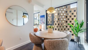 Un'elegante zona pranzo moderna con tavolo rotondo, sedie imbottite, un grande specchio, illuminazione a sospensione e vista panoramica attraverso un'ampia finestra.