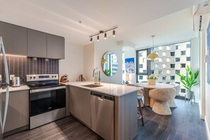 A modern kitchen with built-in appliances, a dining area with a round table, and a view of the cityscape through large windows. - Urban Oasis Balcony Stay | Free Parking & Pool (Montréal)