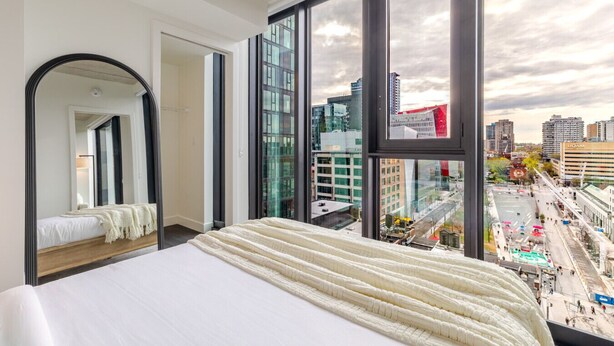 Camera da letto con un letto grande, uno specchio e vista sulla città attraverso ampie finestre.