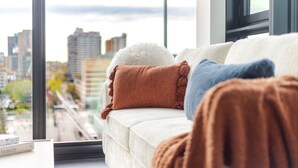 Un divano con numerosi cuscini, una finestra vista sulla città e una lampada.