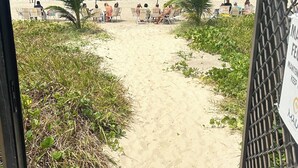 A beach path leading to beach umbrellas and chairs, with a sign indicating maintenance and keeping.