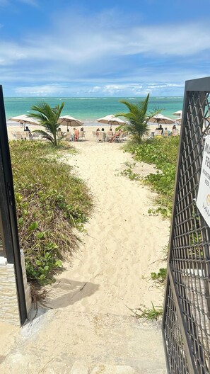 Ein Strandweg führt zu Strandliegen und Sonnenschirmen, mit einem Schild, das auf Instandhaltung und Ordnung hinweist.