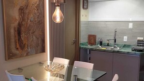 A modern dining area with a glass table and white chairs, a kitchen with a stainless steel sink, and a large abstract painting on the wall.