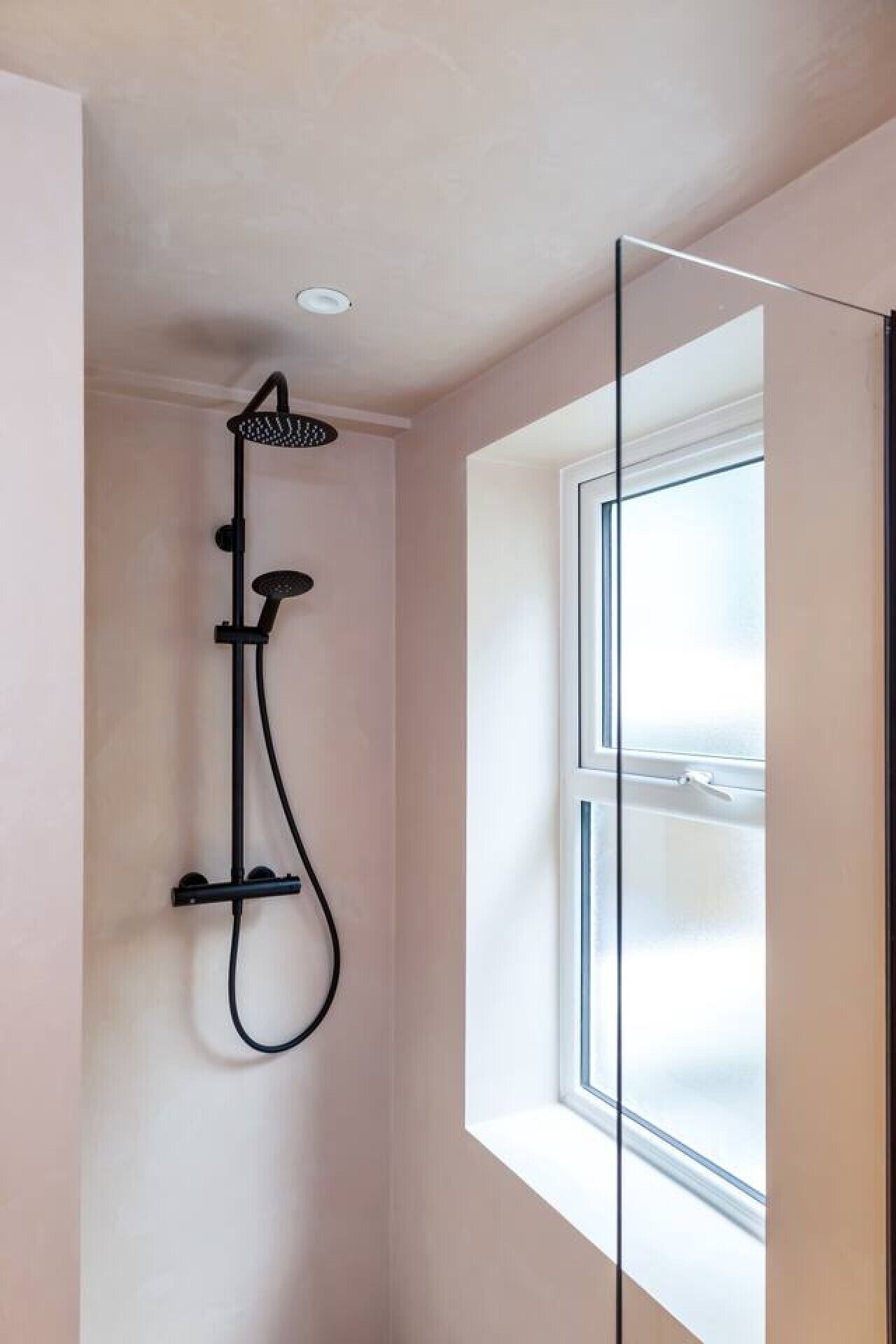 Une douche équipée d’un pommeau de douche à main, d’un panneau de commande fixé au mur et d’une fenêtre avec vue.