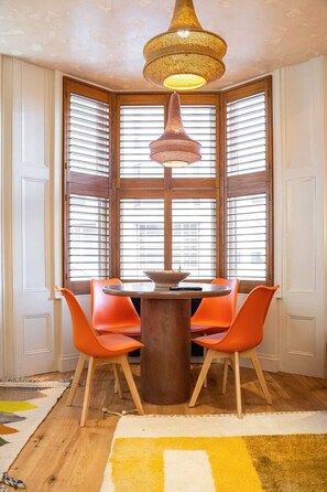 Ein Essbereich mit einem runden Tisch, orangefarbenen Stühlen, einer Deckenleuchte und einem Fenster mit Jalousien.