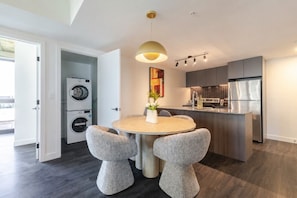 Eine moderne Küche mit integriertem Backofen, einem Kühlschrank und einem Essbereich mit rundem Tisch und zwei Stühlen.
