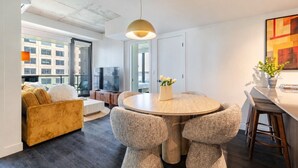 Een moderne woonkamer met een ronde eettafel, zachte zitplaatsen, een televisie en een groot raam.