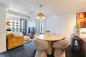 Ein modernes Wohnzimmer mit einem runden Esstisch, bequemen Sitzgelegenheiten, einem Fernseher und einem großen Fenster.