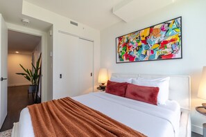 Ein Hotelzimmer mit Bett, einem Bild an der Wand, einer Pflanze und einer Tür zu einem anderen Raum.