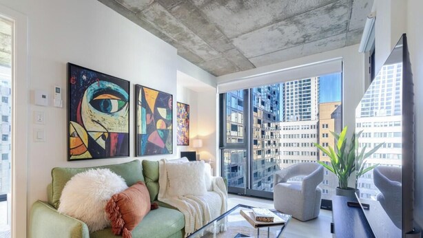 A modern living room with a green sofa, a glass coffee table, and abstract art on the wall. - Executive Apartment | Free Parking & Pool (Montreal)
