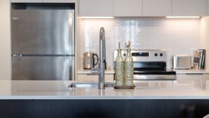 A modern kitchen with a stainless steel refrigerator, a built-in oven, a microwave, and a sink with a faucet. - Executive Apartment | Free Parking & Pool (Montreal)