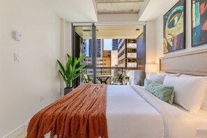 Ein Hotelzimmer mit Bett, kleinem Tisch, Stühlen, einer Topfpflanze und Blick auf die Stadt.