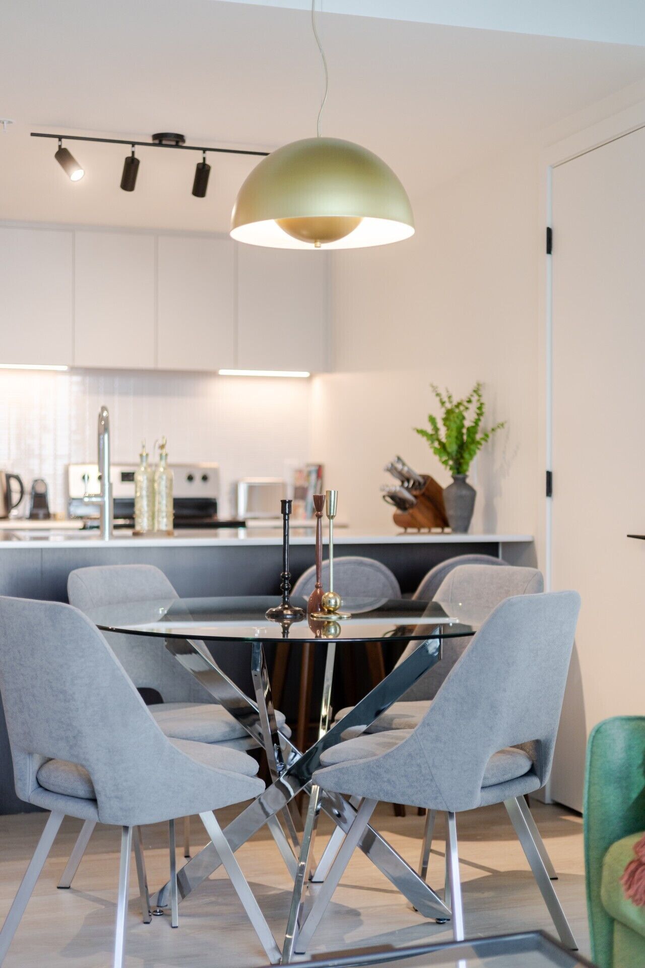 Une cuisine moderne avec des meubles blancs, une table à manger entourée de chaises grises et un luminaire suspendu.
