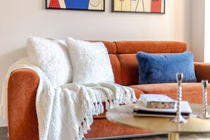 A living room with a sofa, two pillows, a white throw blanket, and a coffee table with books and a decorative item. - Bleury Luxe Retreat | Free Parking & Pool (Montreal)