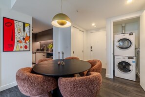 A modern kitchen with a dining area, a washing machine, and a unique abstract painting on the wall. - City View Oasis | Free Parking & Pool (Montreal)