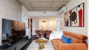 Un salon moderne avec un téléviseur à écran plat, un canapé, une table basse et des œuvres d’art abstraites accrochées au mur.