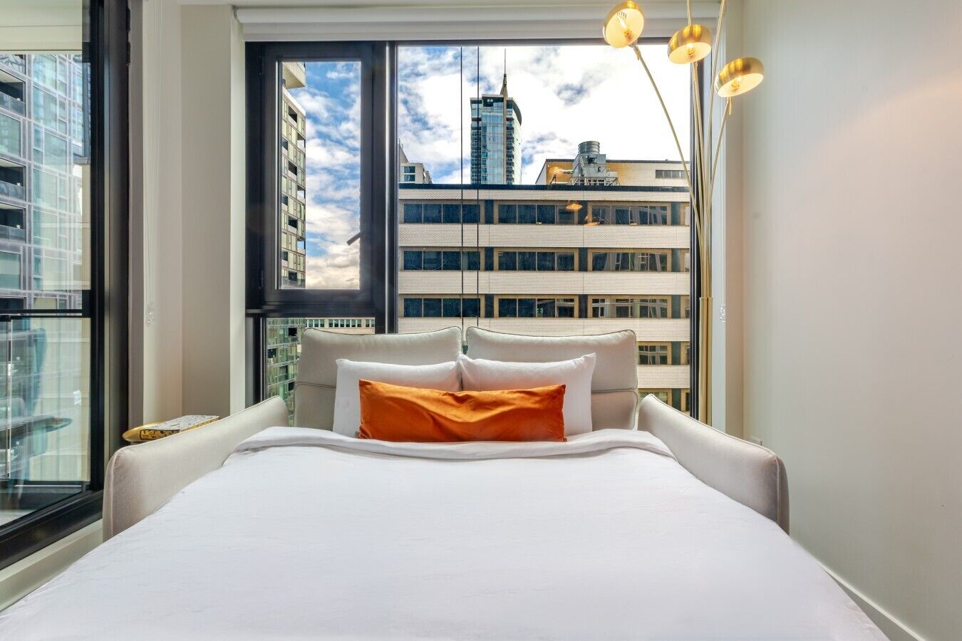 Ein modernes Hotelzimmer mit einem großen Bett, Blick auf die Stadt durch ein großes Fenster und einer stilvollen Pendelleuchte.