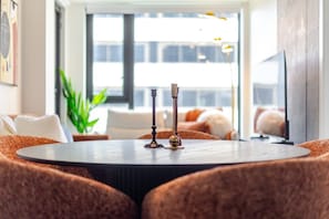 Une table ronde avec deux chandeliers, dans un salon moderne doté d’une grande fenêtre, d’un canapé et d’un téléviseur.