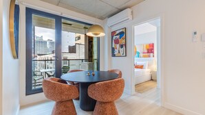 Un'elegante zona pranzo con un tavolo rotondo, due sedie, una lampada a sospensione e vista sulla città tramite ampie finestre.