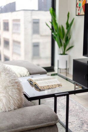 A modern living room with a glass coffee table, a sofa with a fluffy pillow, and a potted plant. - Downtown Comfort Apartment | Free Parking & Pool (Montréal)