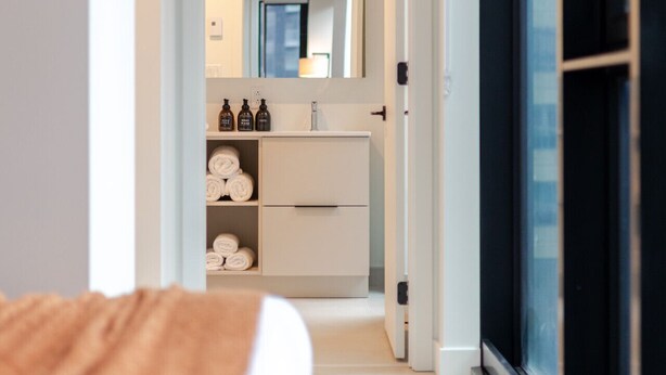 Un corridoio stretto che porta a un bagno con uno specchio, un lavandino e asciugamani.