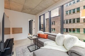 A modern living room with a sofa, a coffee table, a TV, and large windows. - Downtown Comfort Apartment | Free Parking & Pool (Montréal)
