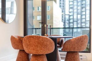 A modern dining area with a round table, two chairs, and a view of a cityscape through large windows. - Downtown Comfort Apartment | Free Parking & Pool (Montréal)