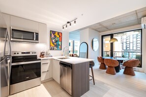 A modern kitchen with stainless steel appliances, a central island, and a dining area with unique chairs. - Downtown Comfort Apartment | Free Parking & Pool (Montréal)