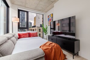 Quarto de hotel moderno com uma cama grande, televisão de tela plana, sofá e vista para a cidade.