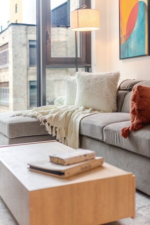 A modern living room with a grey sofa, a white fluffy throw, and a wooden coffee table. - City Luxe Stay | Free Parking & Pool (Montréal)