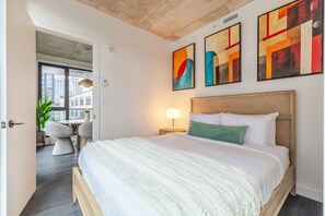 A bedroom with a large bed, a nightstand, a lamp, and abstract art on the wall. - City Luxe Stay | Free Parking & Pool (Montréal)