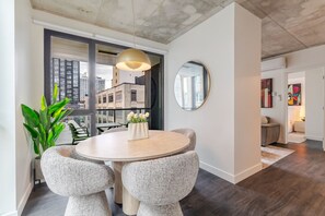A modern interior with a round dining table, two chairs, a potted plant, a pendant light, and a large window with a city view. - City Luxe Stay | Free Parking & Pool (Montréal)