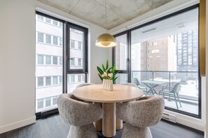 Ein moderner Essbereich mit einem runden Tisch, Stühlen, einer Pendelleuchte und Blick auf die Stadt durch große Fenster.