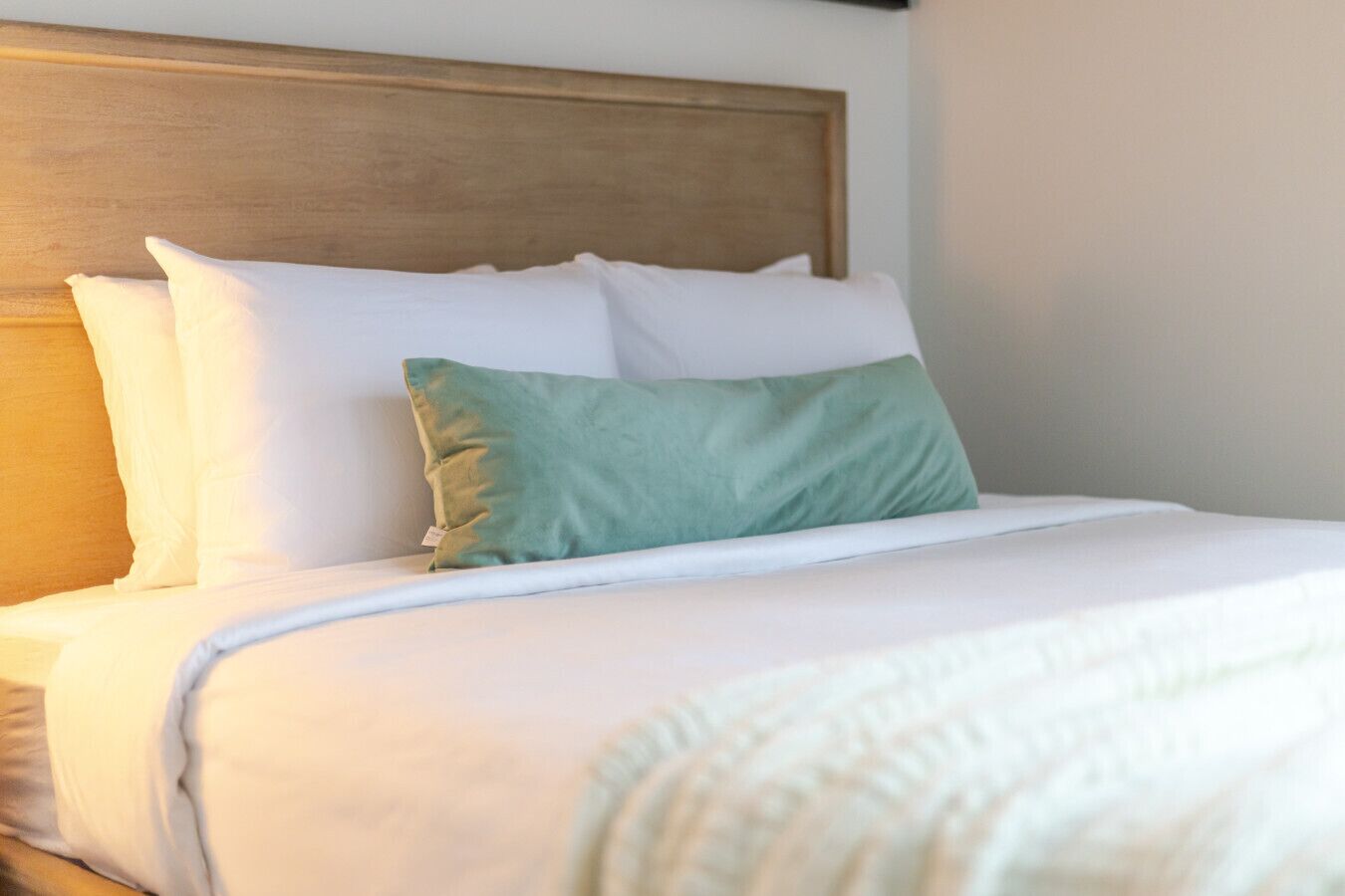 Ein ordentlich bezogenes Bett mit weißen und grünen Kissen, einem Holzkopfbrett und einer weißen Tagesdecke.