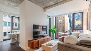 Ein modernes Wohnzimmer mit Flachbildfernseher, Holzmöbeln, einer Couch und großen Fenstern mit Blick auf die Stadt.